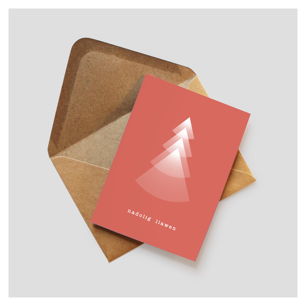 Red greeting card with a minimal linear Christmas tree design. Nadolig Llawen is written underneath the tree in a typewriter style font. The card rests on top of a brown kraft envelope. 