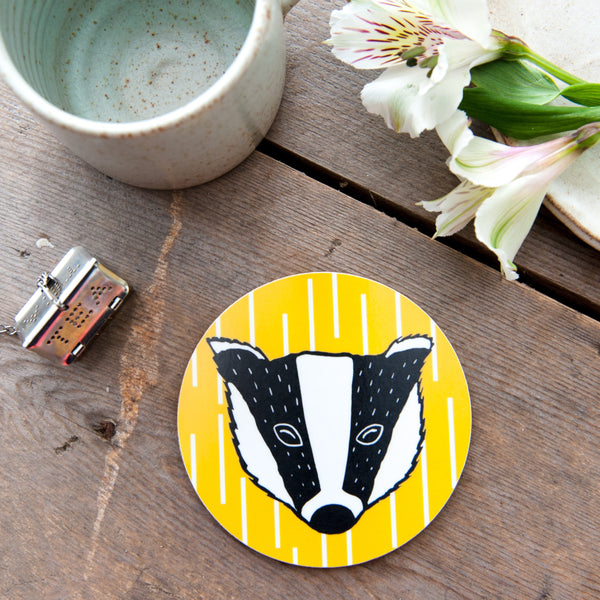 Lifestyle image, round coaster. Yellow and white geometric pattern with black and white badger.