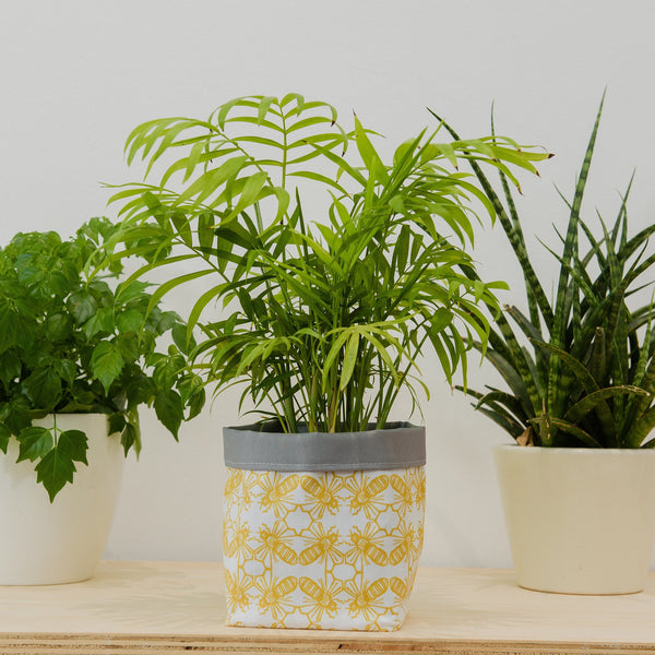 Lifestyle image. Yellow and white geometric bee motif fabric plant pot holder.