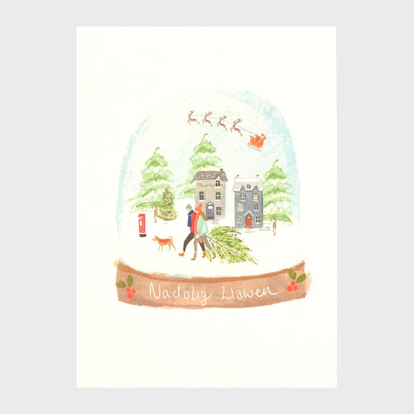 Watercolour and digital illustration on shimmering Pearlescent background. Snowglobe with a wintery scene inside showing a row of houses with snowcapped trees behind them. Santa is flying in his sleigh above the houses. In front a couple dragging a Christmas tree walk with their dog. 