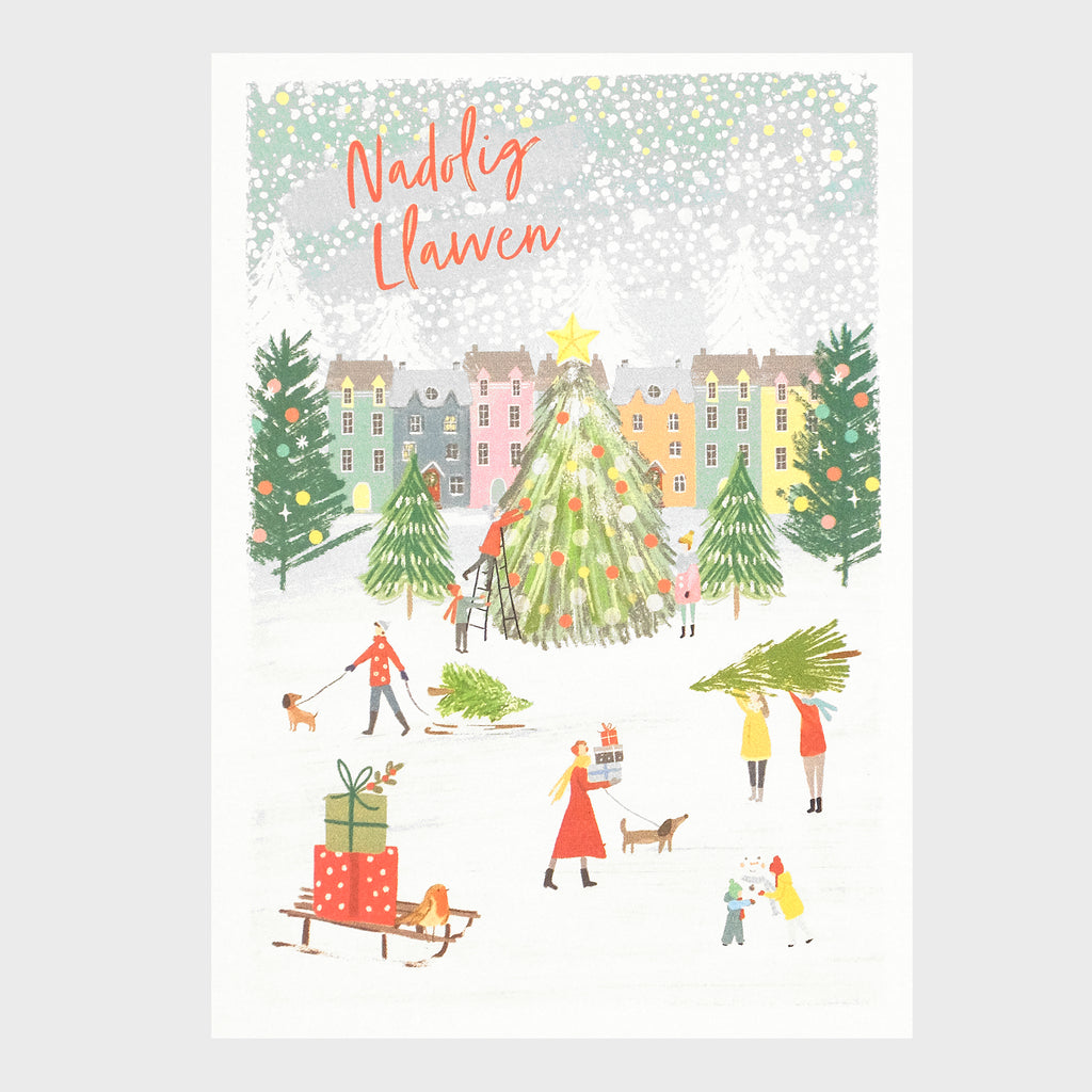 Watercolour and digital illustration on shimmering Pearlescent background. Featuring a town centre with row of houses in the background. The ground is covered in snow and there is snow falling. People are decorating a big Christmas tree in the centre of the card whilst other people walking dogs and carrying trees are in the foreground.