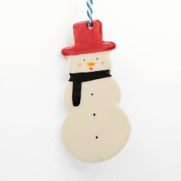 Ceramic hanging decoration. Snowman wearing a black scarf and red hat. It has three black coal buttons down its centre. Pink cheeks and an orange round nose