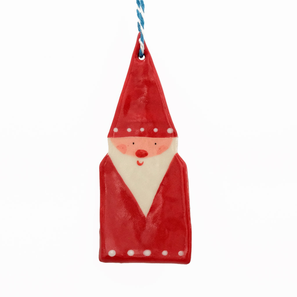 Ceramic hanging decoration. Santa wearing a pointy santa hat with white dots on the brim, and white dots along the base of his red coat. He has a long pointy white beard and rosy pink cheeks. 