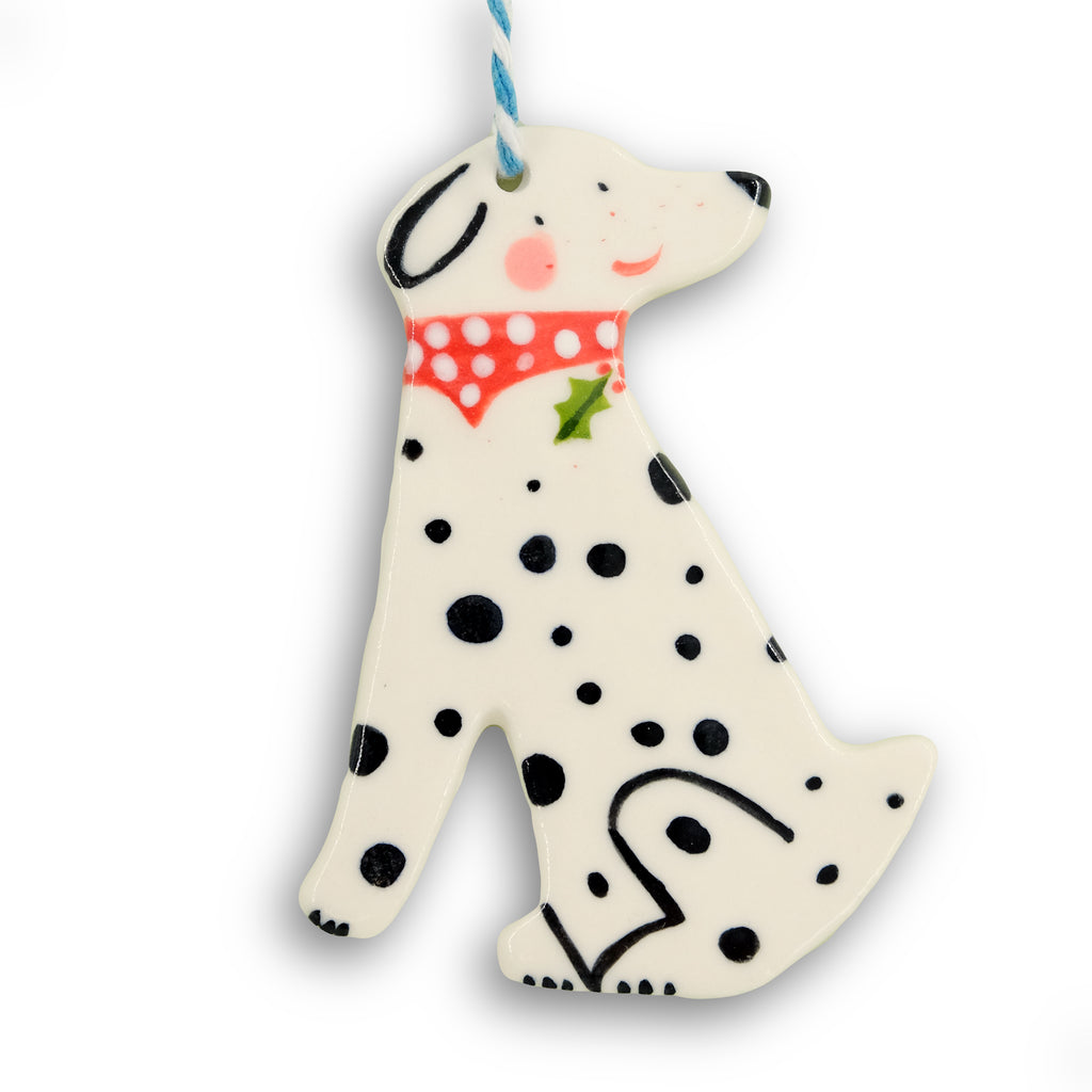 Hanging Christmas decoration. Black and white Dalmatian dog in side profile, wearing a red and white polka dot bandana as a collar with a sprig of holly. Hangs from blue and white twine. 