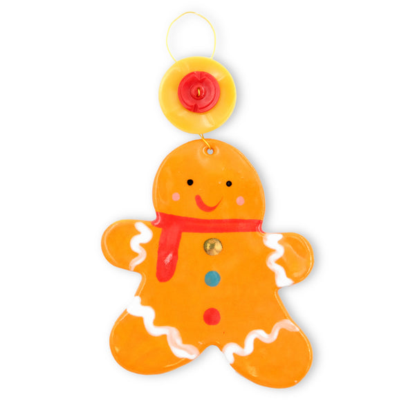 Ceramic hanging decoration. Gingerbread person wearing a red scarf with white icing style cuffs its legs and arms. Three colourful blobs as buttons down its front. It has a bright yellow button with a smaller red button on top attached to the gold coloured hanging wire above its head. 