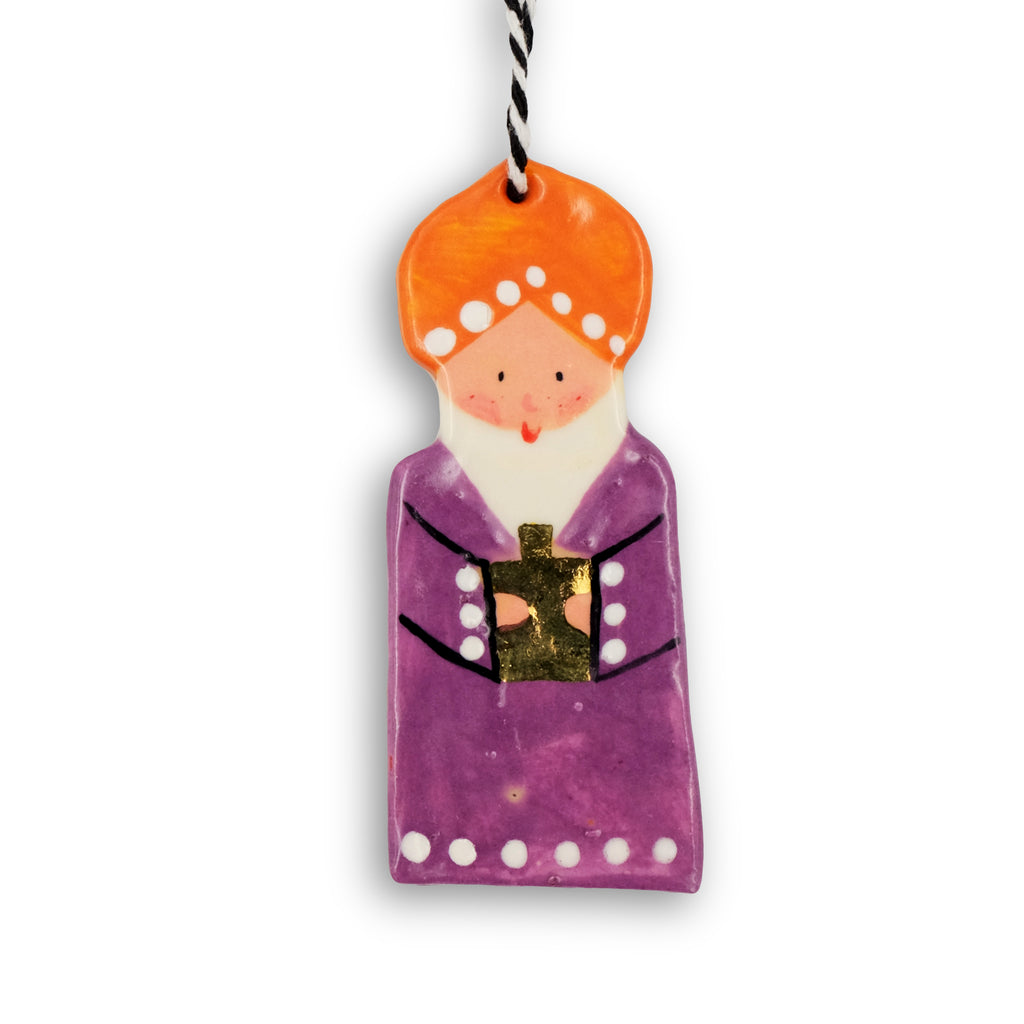 Ceramic hanging decoration. Wiseman carrying a golden bottle. Wearing an orange turban and purple robe with white dots. 