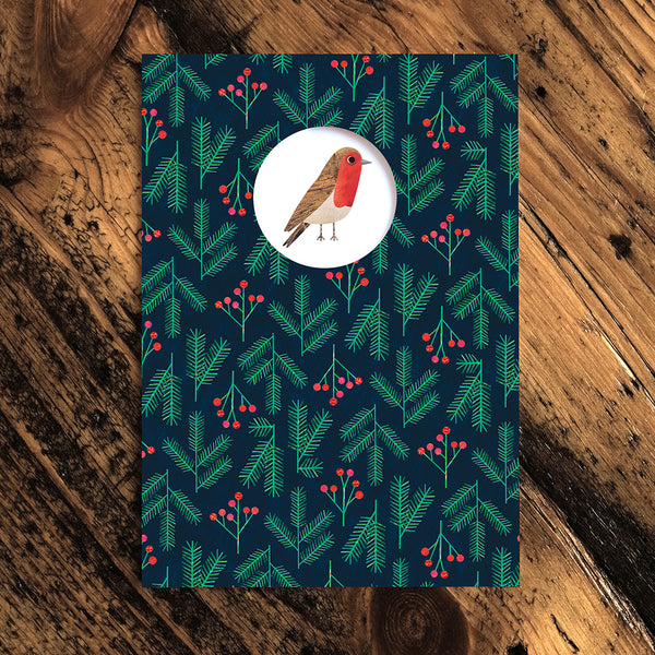 Christmas card, navy background with graphic fir branch and berry pattern. white circle cut-out with an illustration of a robin. 