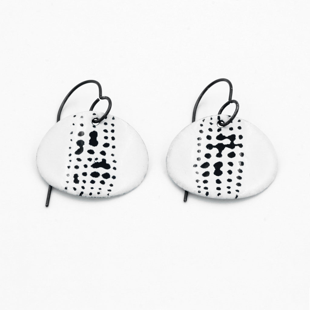 White enamel oval drop earrings with mark details in black. Hoop fastening. 
