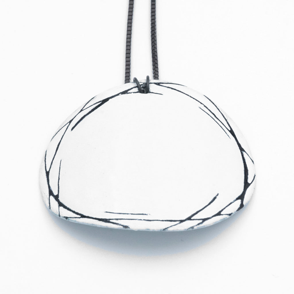 White enamel marked pendant. Large curved oval feature with black markings etched around the border. 