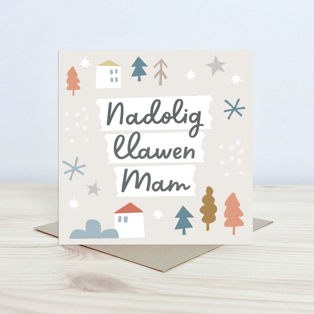 Christmas Card with the text 'Nadolig Llawen Mam' featured on the front in black cursive font on a white background. The background is pale cream with graphic block houses, stars, snowflake and tree shapes. 