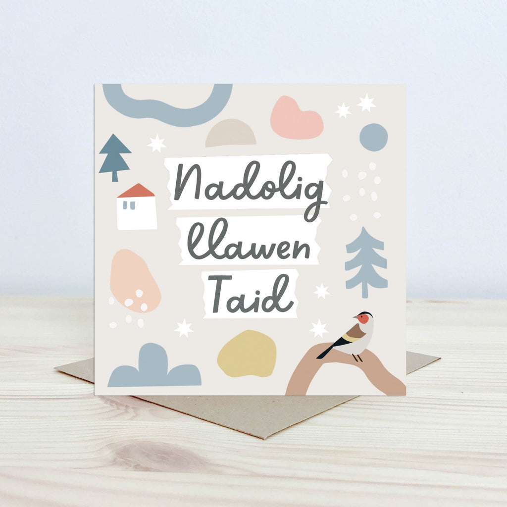 Christmas Card with the text 'Nadolig Llawen Taid' featured on the front in black cursive font on a white background. The background is pale cream with a bird on a branch in the foreground and graphic stars, snowflake and tree shapes. 
