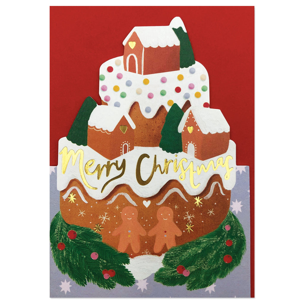 The card is die cut and embossed with gold foil detailing. The card shows an illustration of a Christmas cake topped with Gingerbread houses, people and Christmas trees. There is Christmas foliage around the base of the cake. 
