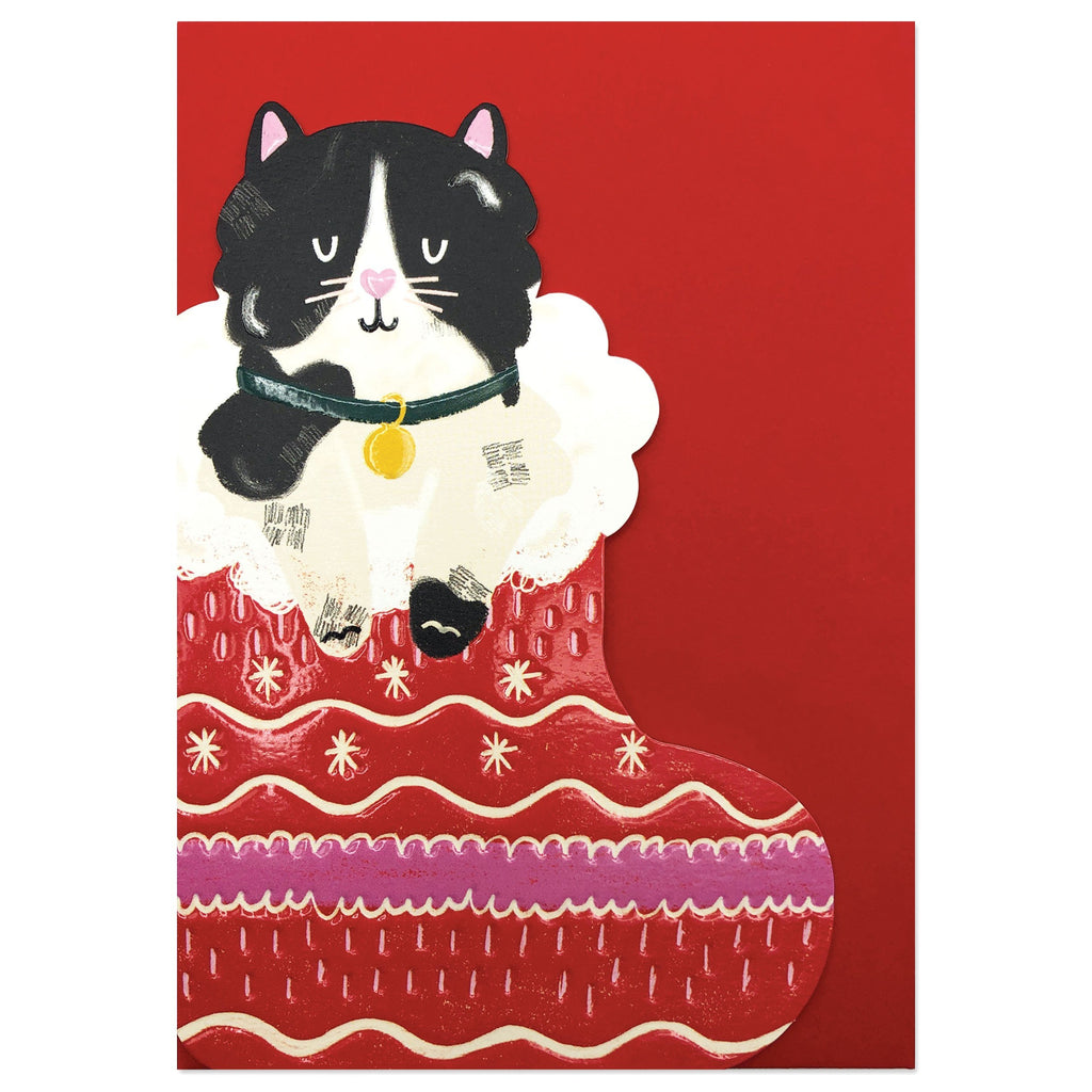The card is die cut and embossed. It shows an illustration of a black and white cat sat inside a pink and red festive stocking with a fluffy white trim. 