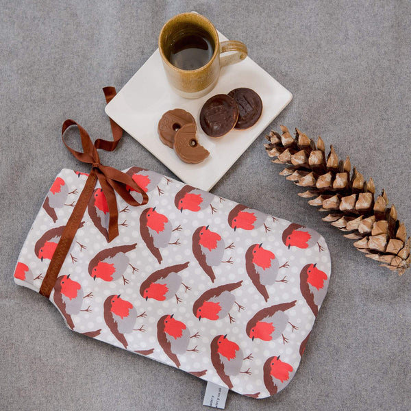Lifestyle image.  Patterned fabric hot water bottle with robin motif and brown ribbon.