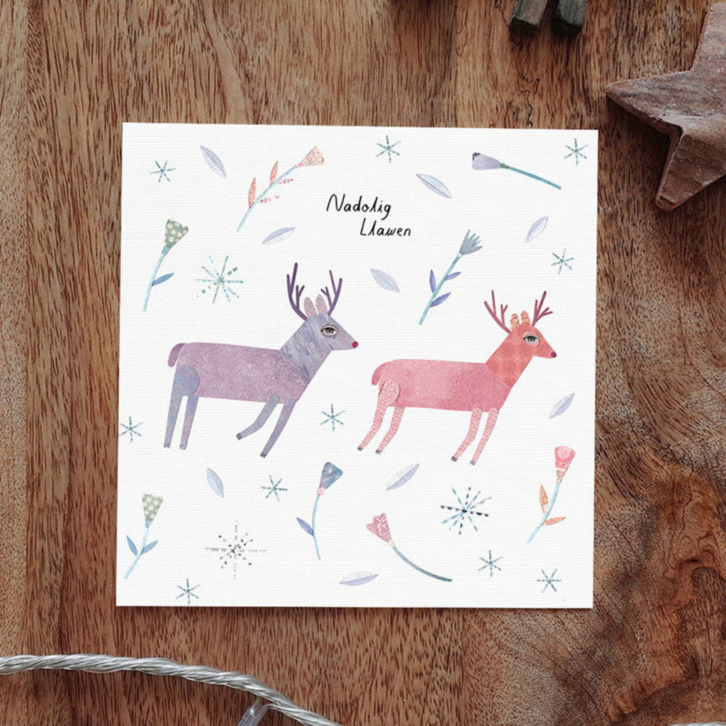 Collage style illustration with a white backgroun showing two reindeer amongst a background of falling snowflakes and festive foliage.